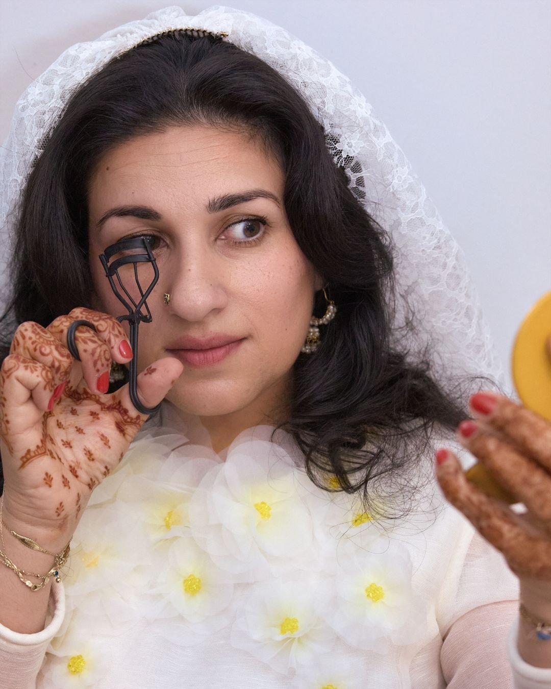Kirin Bhatty wearing a wedding outfit and curling her lashes.