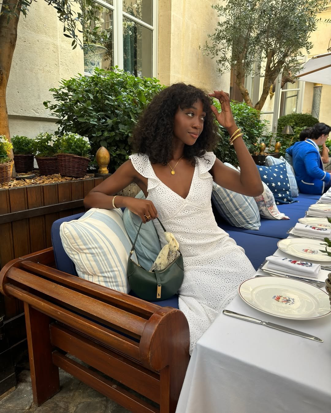 @emmanuellek_ wears a white broderie dress with ruffle sleeves while she sits at a Parisian restaurant