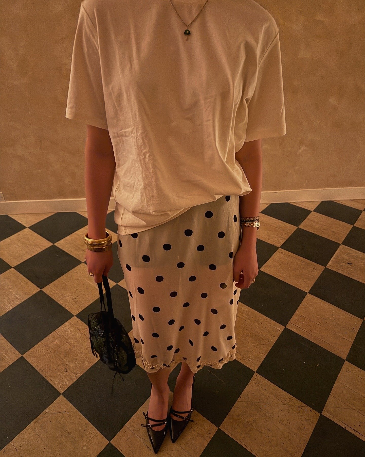 A woman wearing a sheer polka dot skirt, a white tee, and black pointed-toe kitten heels.