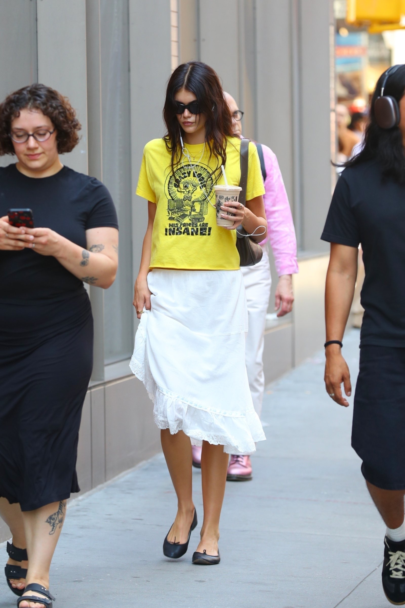 An image of Kaia Gerber wearing a linen skirt with yellow vintage t-shirt and black ballet flats while out in New York.