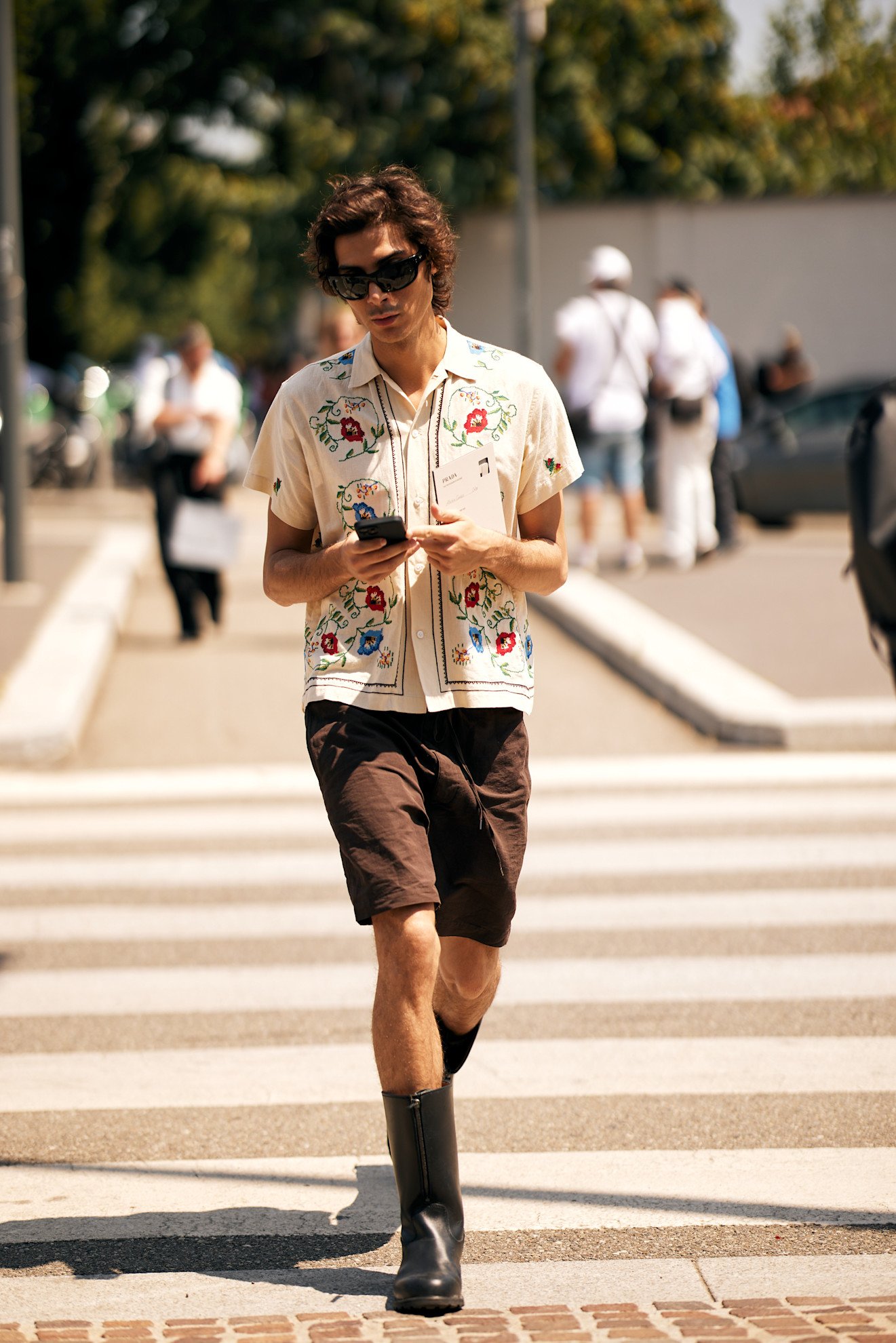 Mens Fashion Week SS26 showgoer wearing a blue shirt tucked into a brown textured miniskirt with brown rope sandals and a black tote bag.