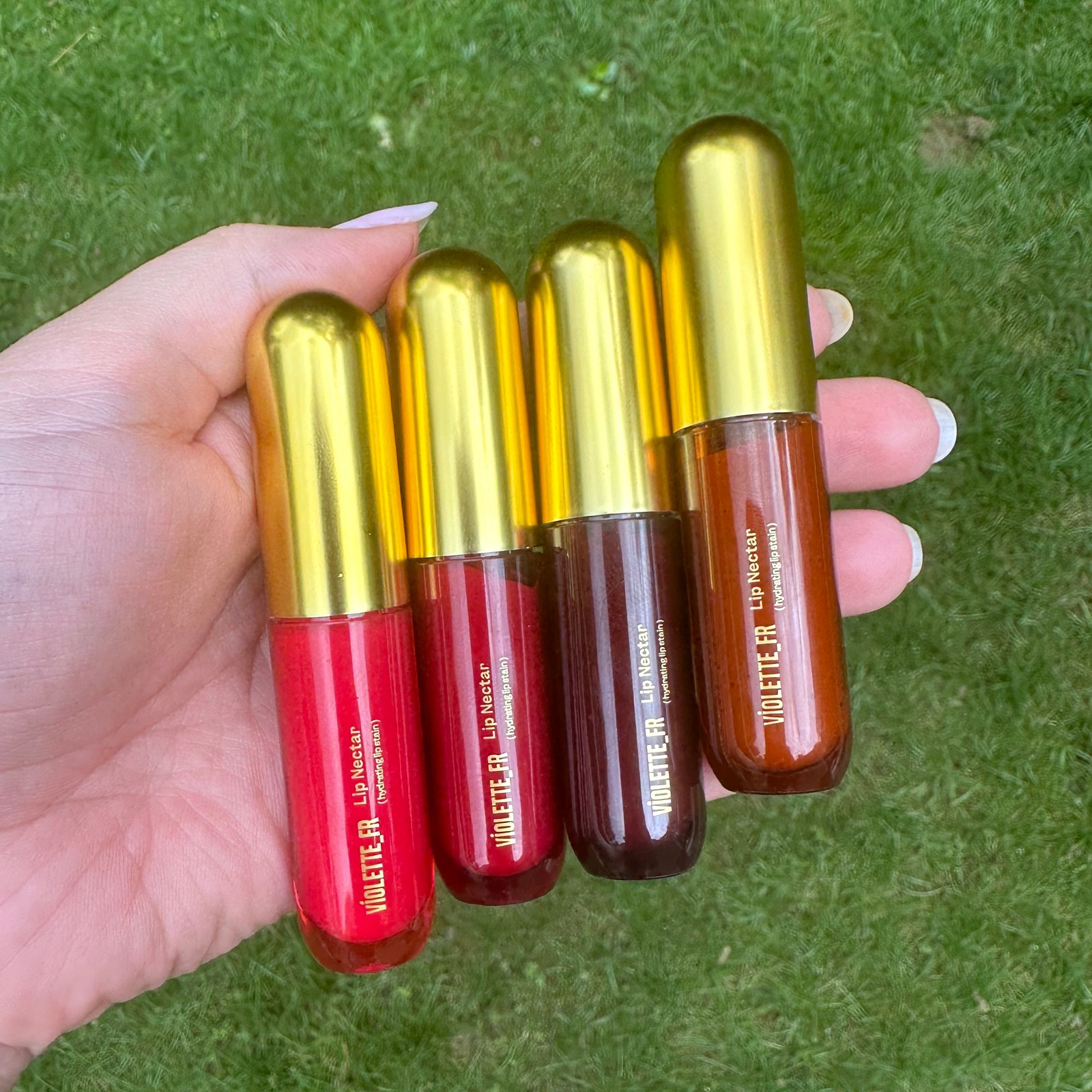 Person holding Violette_FR Lip Nectars in four different colors.