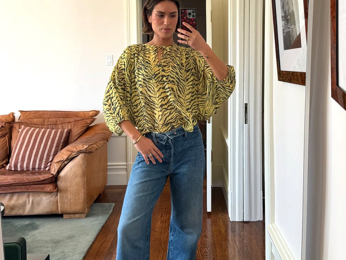 Caitlin Miyako wearing wide-leg denim jeans, green and black animal print blouse, and black ballet flats.