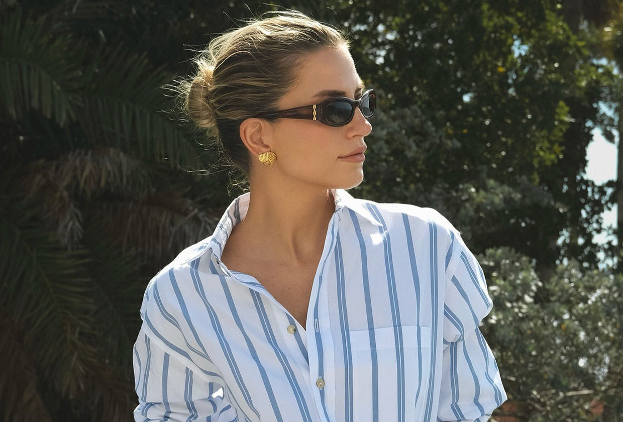 Influencer wearing sunglasses, striped button-down shirt, and white linen pants.