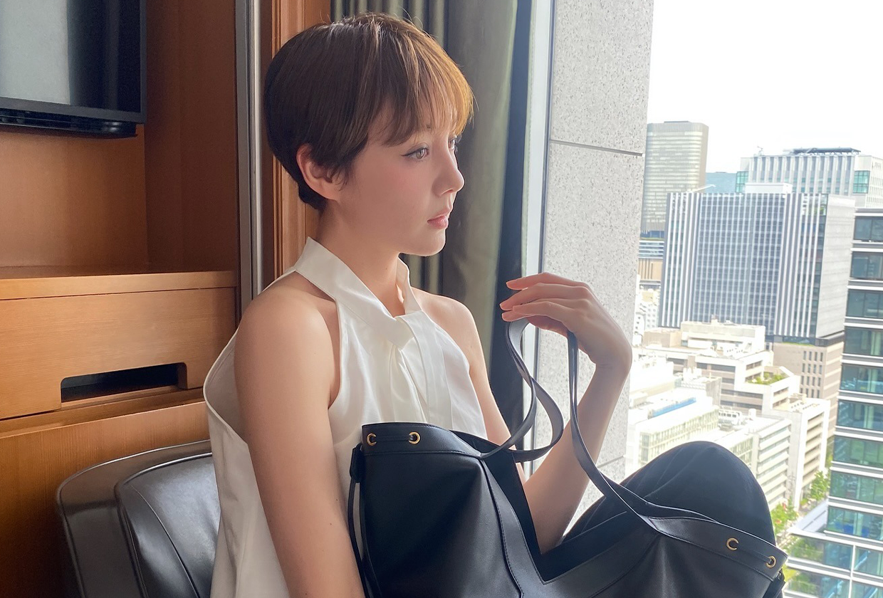 Photo of Reina Triendl wearing white cotton poplin shirt, jeans, and black bag while in Tokyo hotel room.