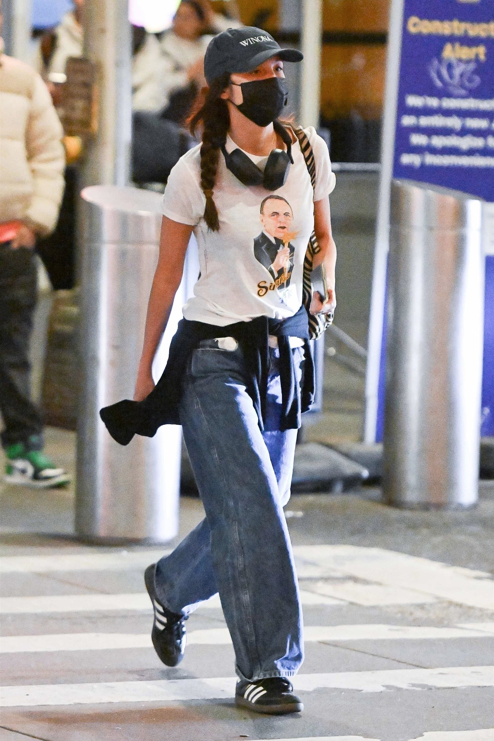 Olivia Rodrigo spotted arriving at JFK airport in New York City wearing a Frank Sinatra 1979 Tour shirt, a Winona hat, blue barrel jeans, and Adidas sneakers.