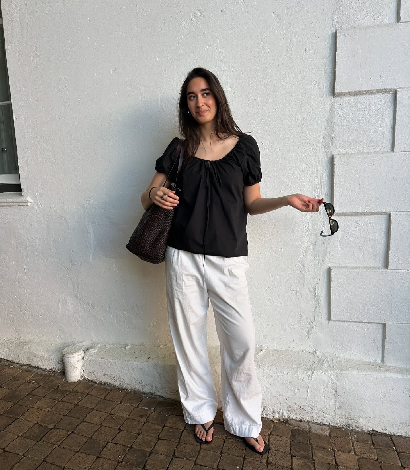 Influencer Selena wearing white trousers and a black scoop-neck blouse.