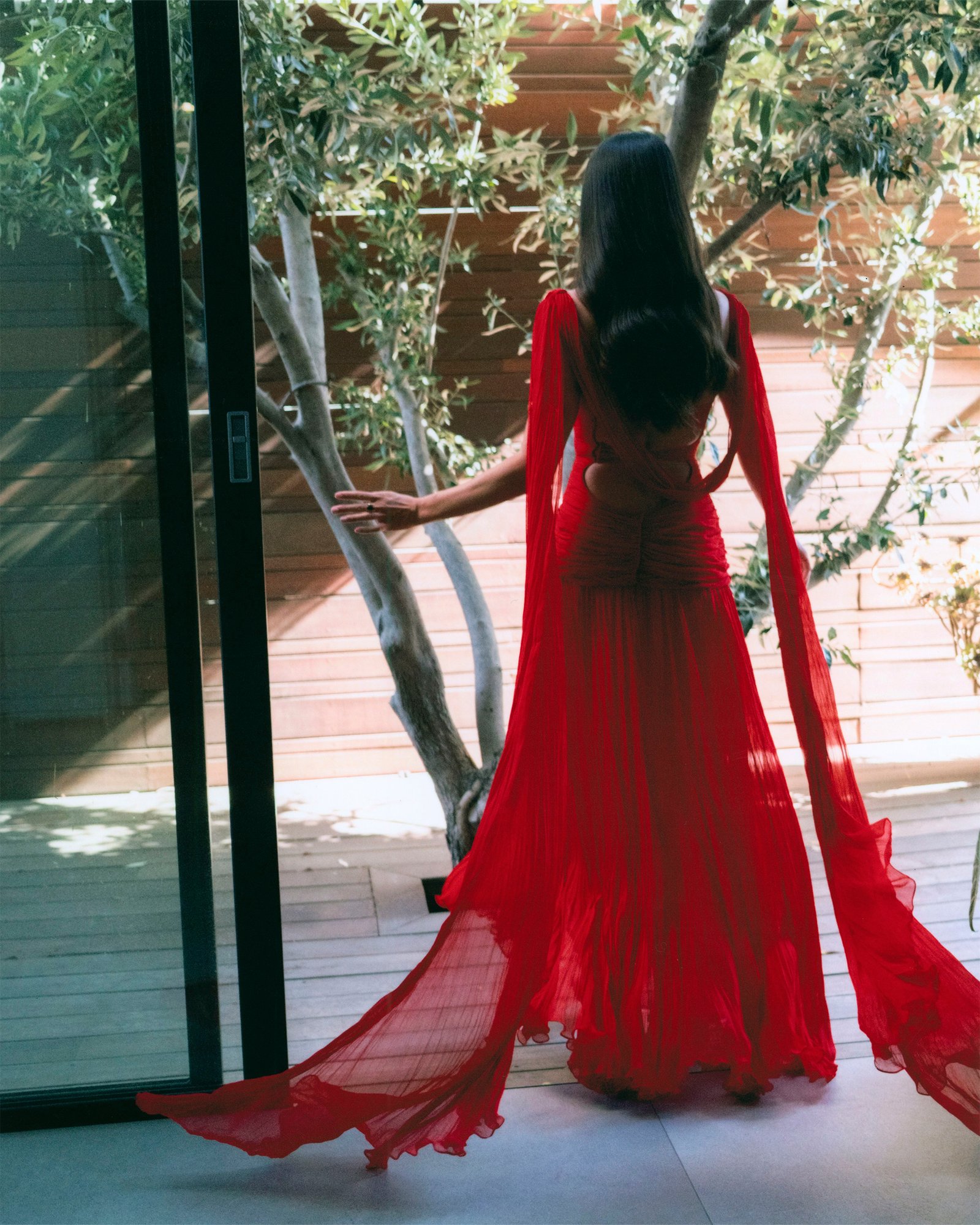 Photo of Sara Sampaio in her final look before the Superman Los Angeles premiere. She is turned away from the camera wearing a red Marmar Halim gown.