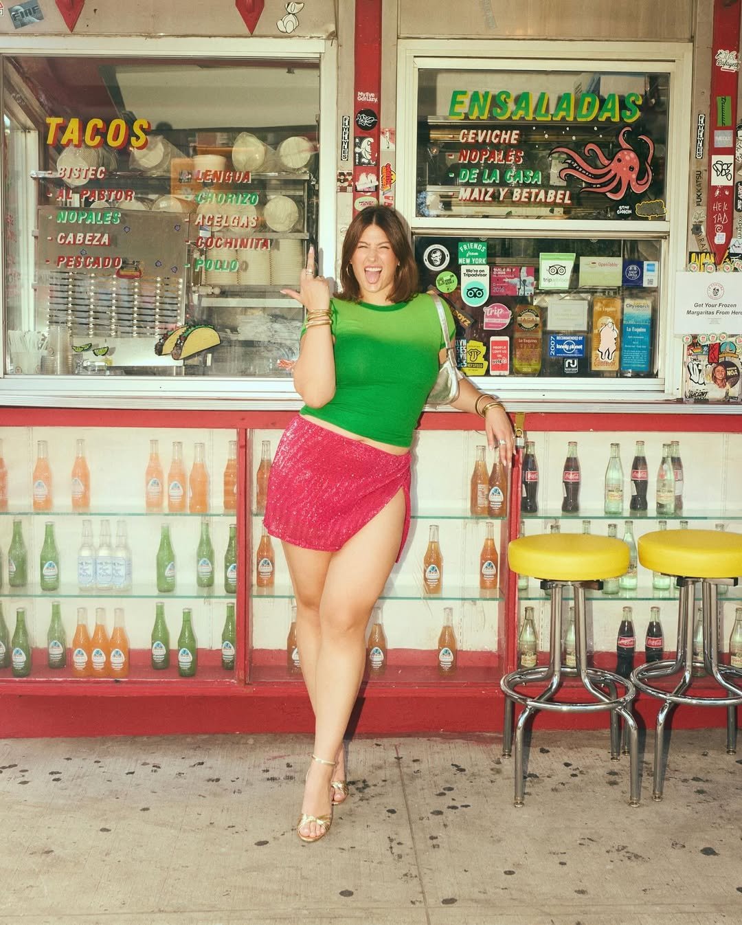 Fashion person Reaann Langas is wearing sequin skirt, green top and matching bag and shoe combination in gold. She is stood in front a taco stand swearing at the camera in a recent image from her Instagram.