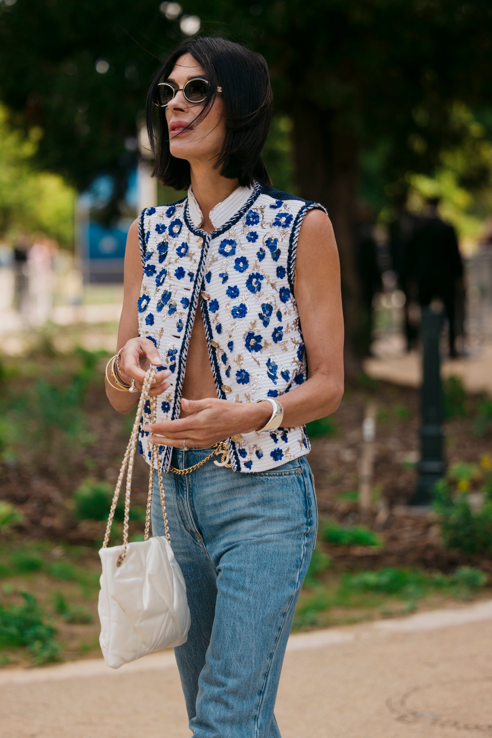 Guest wearing a Chanel vest, jeans, and a white Chanel bag to FW24 Chanel Haute Couture show in Paris.