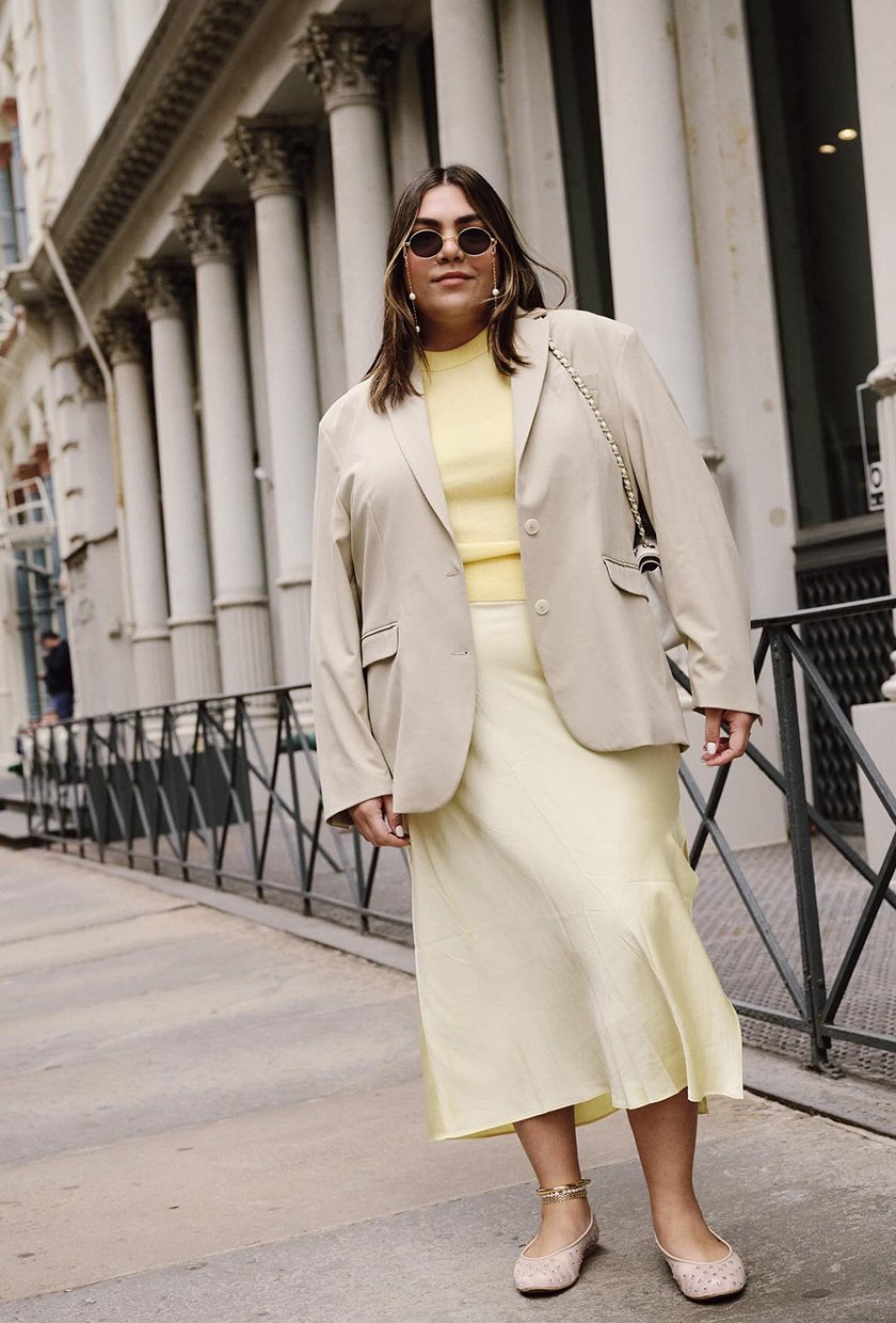 a photo of a yellow outfit for summer with a woman wearing a tan blazer over a yellow sweater with a yellow slip skirt and mesh ballet flats