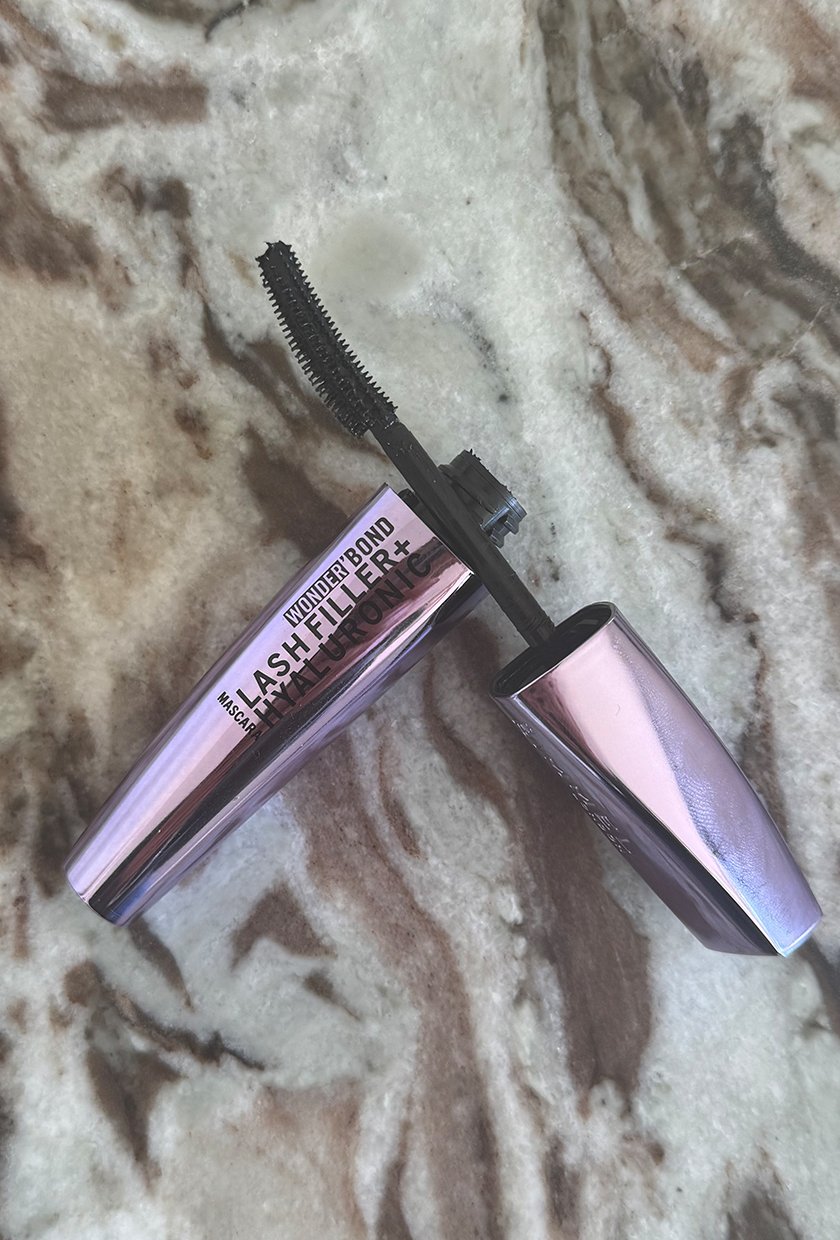 The Rimmel Wonder'Bond Lash Filler + Hyaluronic Mascara wand resting on the tube on a marble table