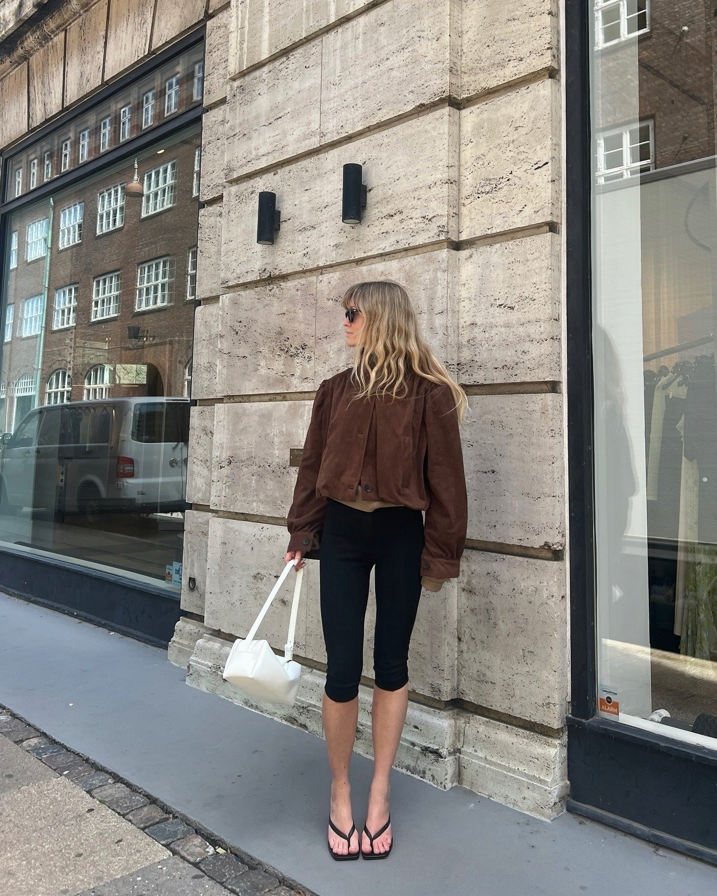European influencer wearing a brown suede jacket, capri pants, and kitten heel flip-flops