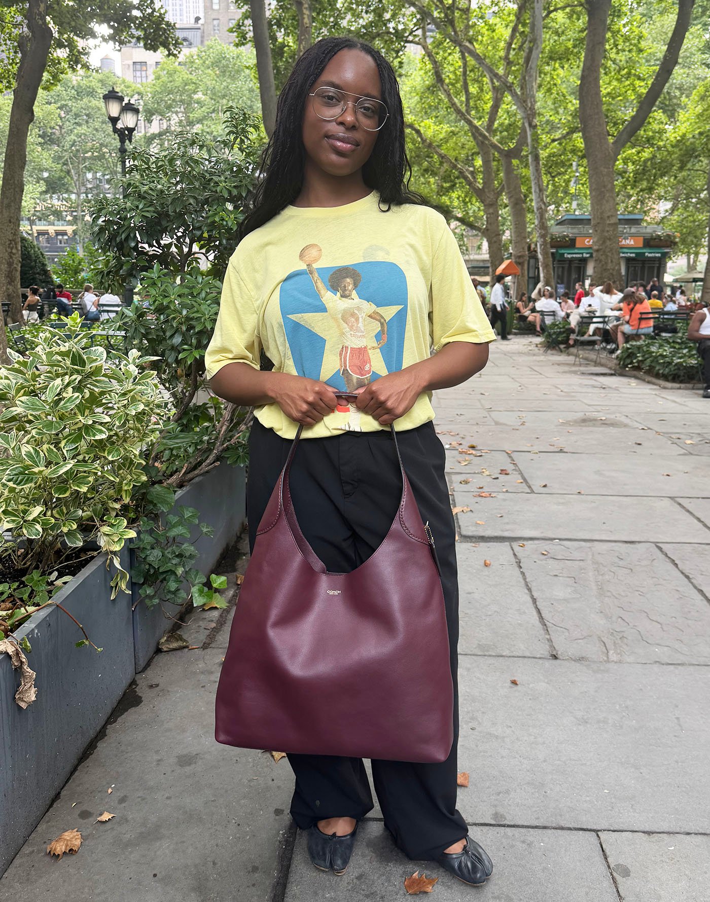 A woman wearing a yellow T-shirt, black pants, and a Coach burgundy Brooklyn Shoulder Bag