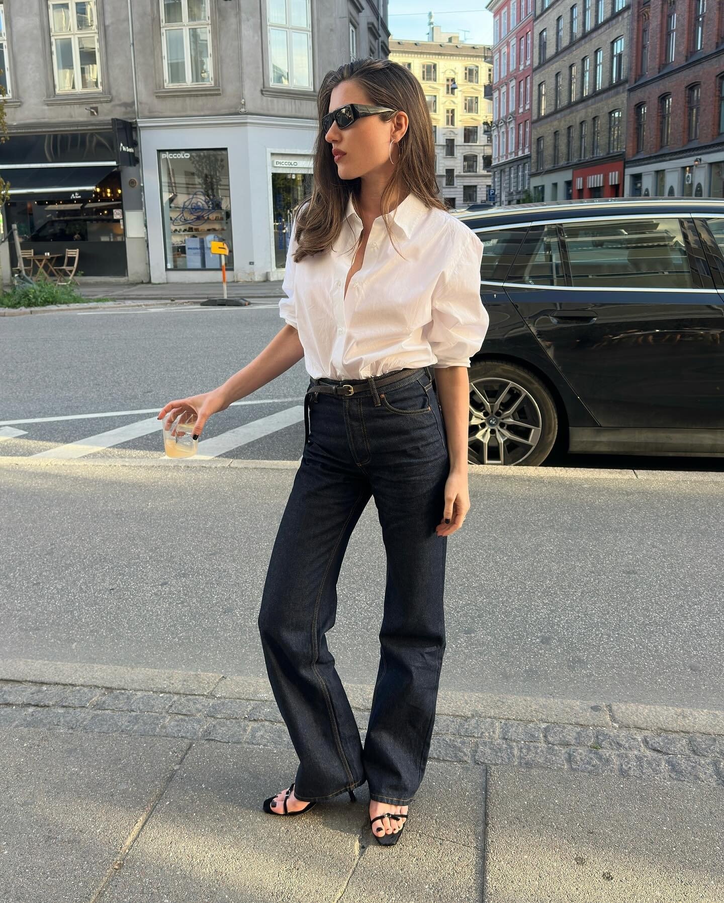 @iliridakrasniqi wearing a white button-down shirt with flare jeans and sandals.