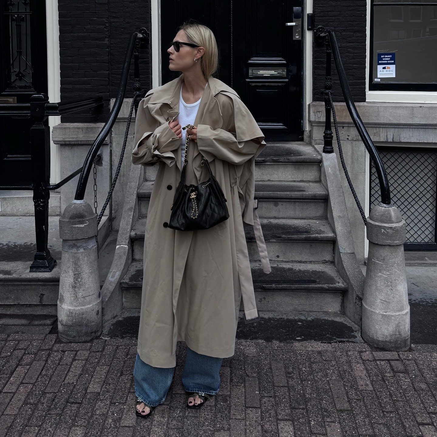 @lindatol_ wearing a white tee, trench coat, and wide-leg jeans.