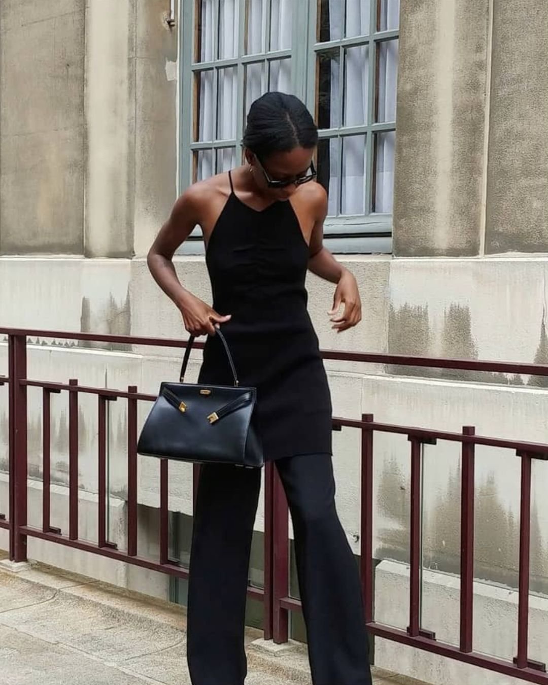 Influencer @sylviemus_ wears a black longline sleeveless top over black satin trousers with a glossy black leather handbag.