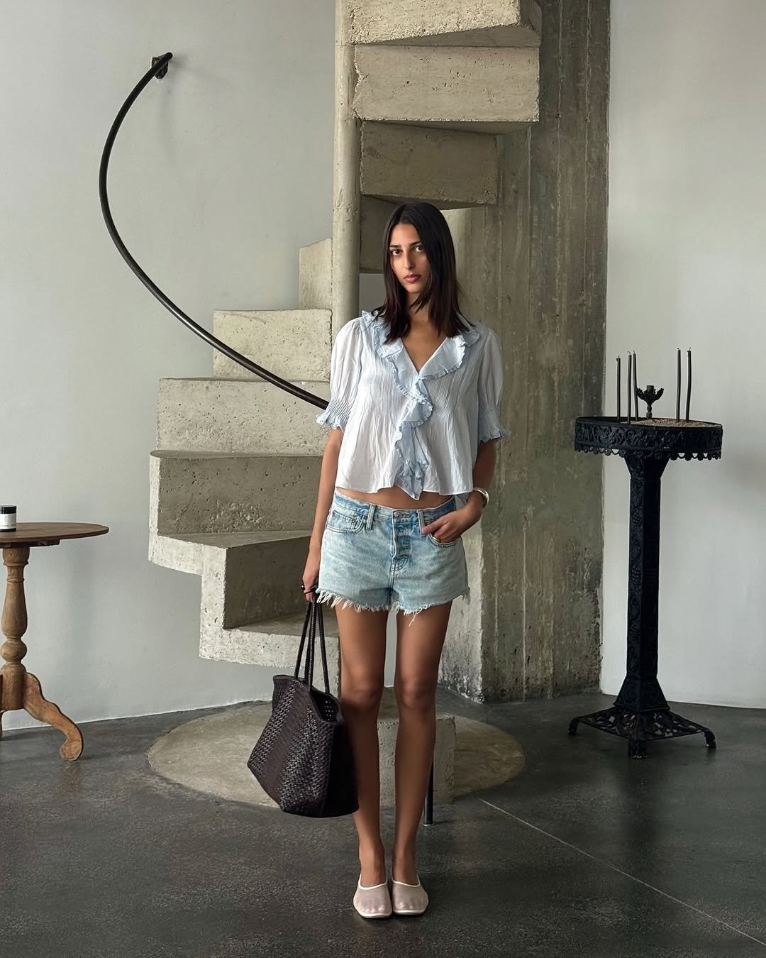 Influencer wearing denim shorts with a ruffled blouse and mesh flats