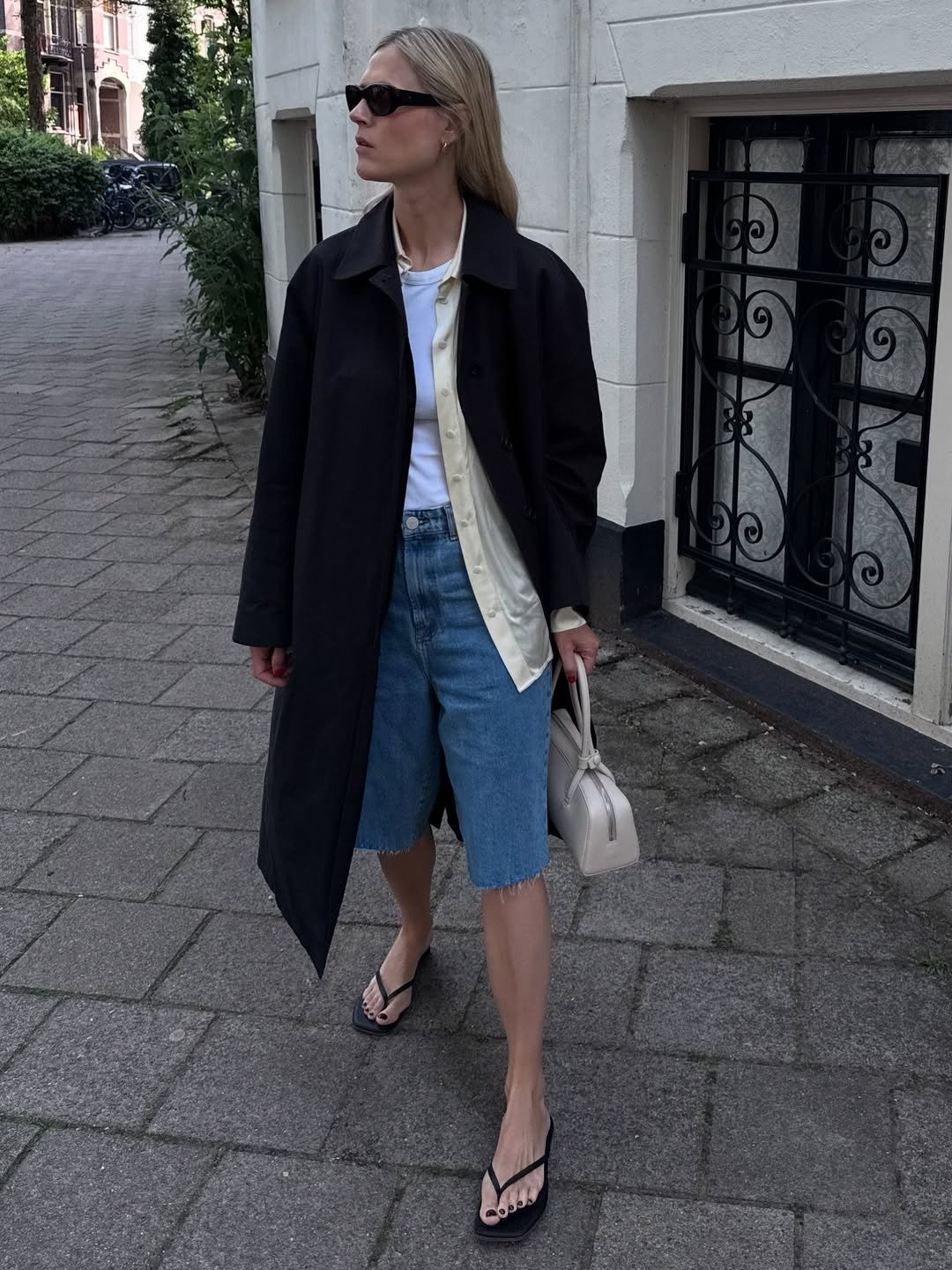 Influencer wearing denim shorts with a trench coat and flip-flops