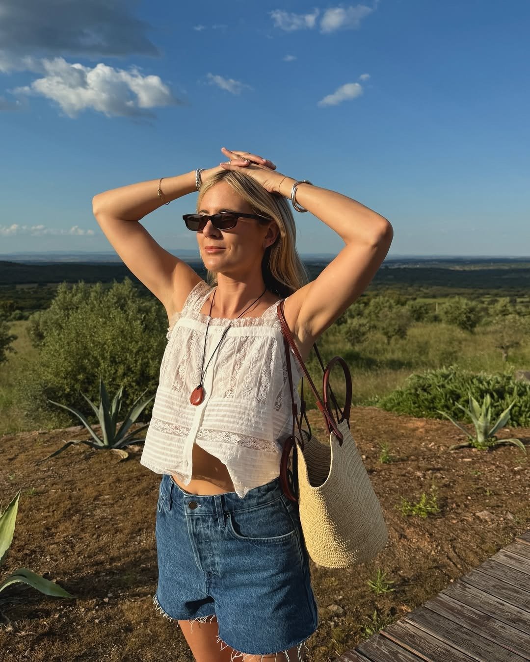 Influencer wearing denim shorts with a white eyelet top and raffia bag