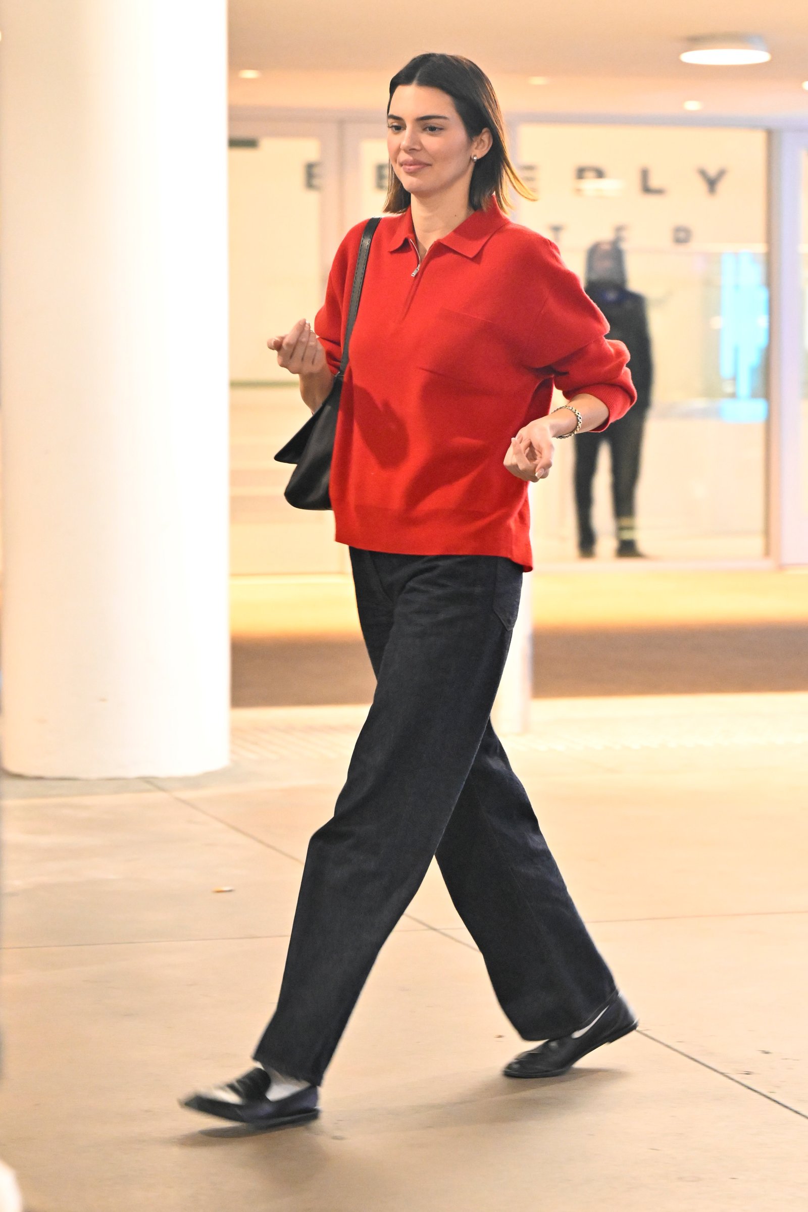 An image of Kendall Jenner wearing a red half-zip long-sleeve polo top from The Row with trousers and loafers.
