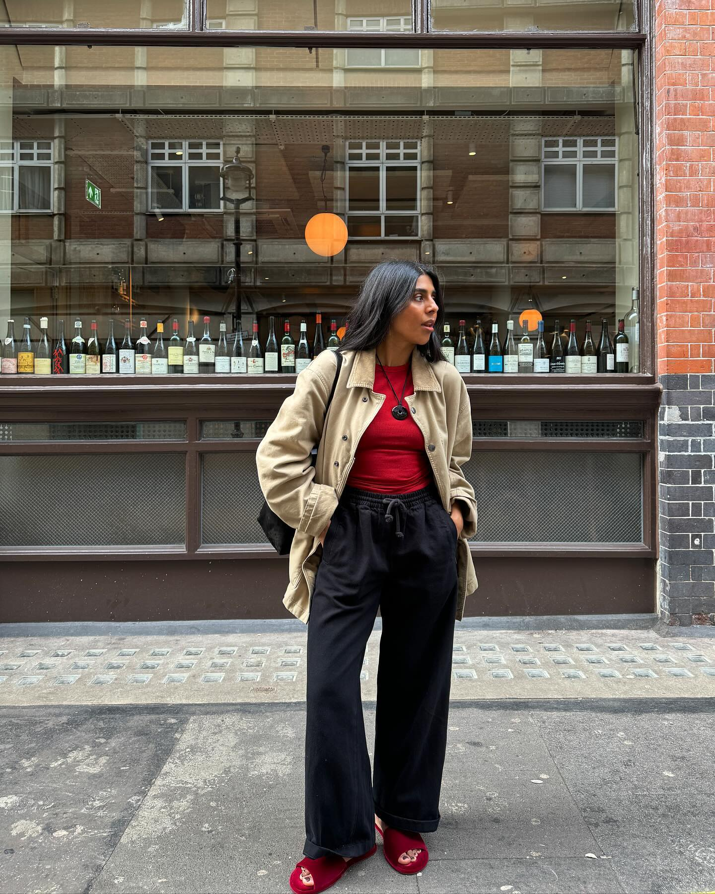 An image of @monikh wearing a red top with black joggers, red sandals and a beige jacket while in London.