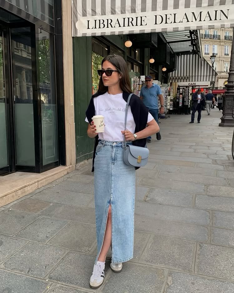 @leasy_inparis wears a denim maxi skirt with trainers, a white T-shirt and a navy jumper knotted round her neck