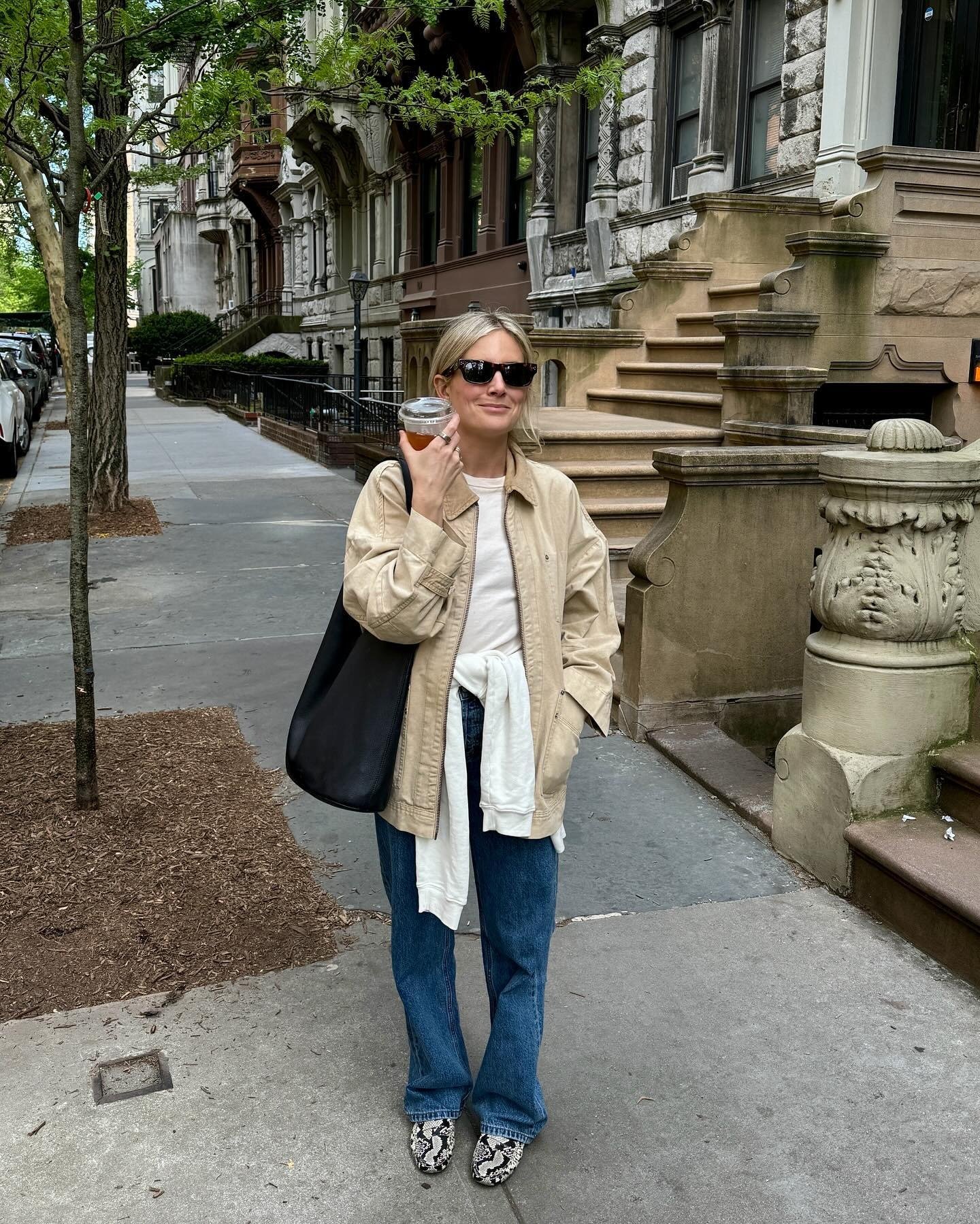 Influencer @lucywilliams02 wears blue slouchy jeans with snake print loafers, a white tee, a beige barn jacket and a black tote bag. She stands outside on the street in New York.