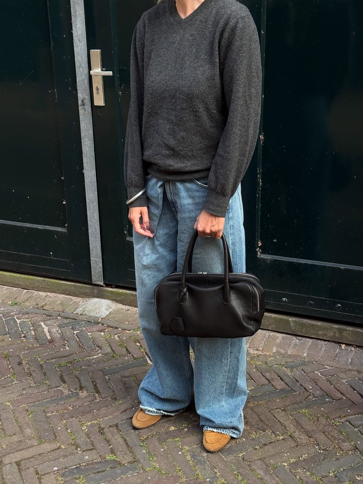 Influencer @lindatol_ wears slouchy jeans with a grey jumper and a black leather east-west bag.