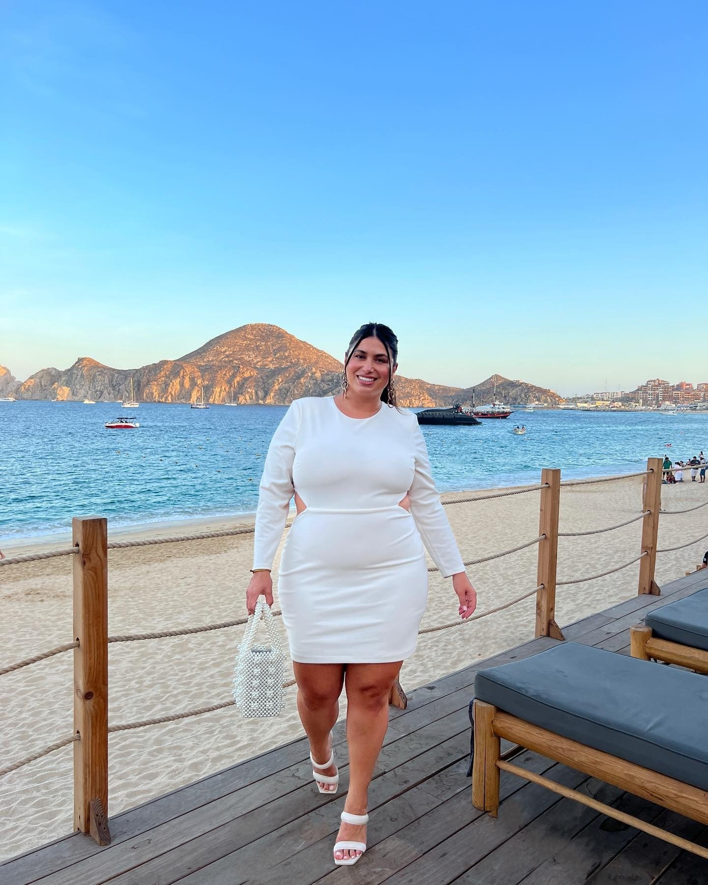 Plus size bride wearing white mini dress while on beach.