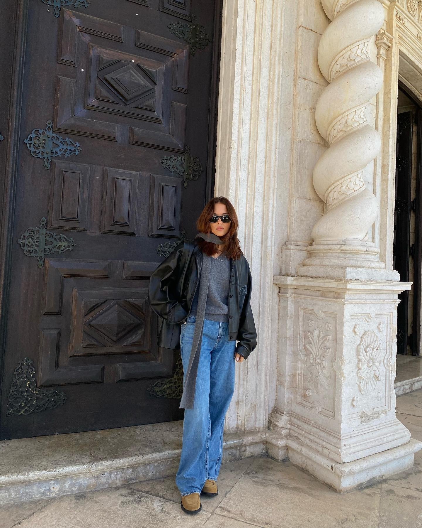 Influencer @deborabrosa wears slouchy jeans and suede loafers with a grey jumper and a black leather jacket.